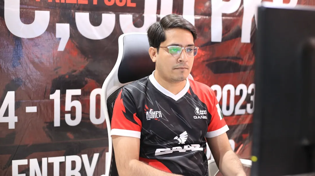 A CS:GO player in a team jersey at a competitive tournament, prize-pool banner visible behind him